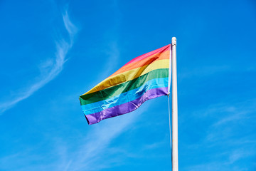 Rainbow flag against a blue cloudy sky.
