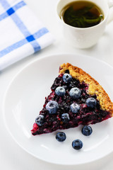 Slice of pie with black currant and blueberries and a cup of tea