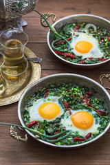 Green shakshuka. Fried eggs with fresh spinach, ramson, leek in a pan on a gray background, top view