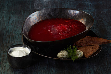 Dish from the menu of the restaurant a plate of red borsch with beets with bread, bacon and sour cream on a dark green wooden background