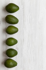 Whole avocados on white wooden table, top view. Overhead, from above. Copy space.