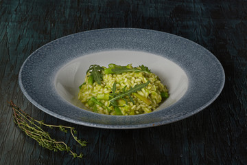 Dish of restaurant menu risotto with green asparagus and rucola on a beautiful dish on a green...