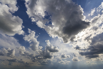 Fantastic panorama view of bright white puffy clouds lit by sun spreading against deep blue summer...