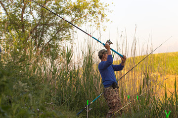 Fisherman with a fishing rod on the river bank. A fisherman is fishing. Fish, rotating coil. - The concept of rural recreation. Article about fishing.