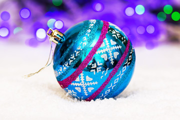 beautiful ball for Christmas tree decoration lies on artificial snow on bokeh background