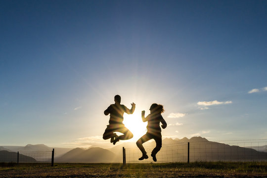 silhouette couple jumping happy with backgroud sun and mountains