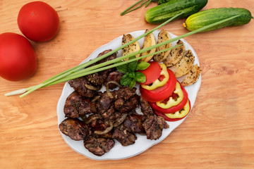 Dish with chicken liver, stewed with apples and onions, decorated with slices of sweet pepper and tomatoes, next to the table ripe whole tomatoes, cucumbers and a sprig of basil.