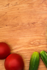Cucumbers and tomatoes on a wooden background, top view, vertical frame.
