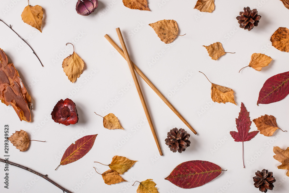 Wall mural Autumn background: autumn leaves and asian chopsticks hold pinecone. Top view, flat lay.