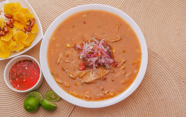 Above view of traditional Ecuadorian food called Encebollado, fish stew and ring onions inside, served with popcorn, chifles, lemon and red sauce inside of bowl
