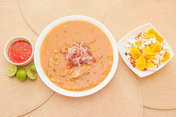 Above view of traditional Ecuadorian food called Encebollado, fish stew and ring onions inside, served with popcorn, chifles, lemon and red sauce inside of bowl