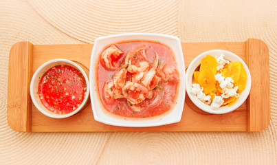 Above view of delicious shrimp cebiche in rectangular white bowl served with chifles and red spicy sauce over a wooden structure in table background