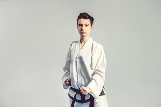 girl in karate suit kimono in studio at grey background. Female child shows judo or karate stans in white uniform with black belt. Individual martial art sport . body portrait