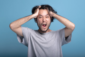 Young bearded man excited shocking pose in blue background.
