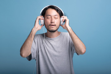 Young bearded man listening to music in blue background.