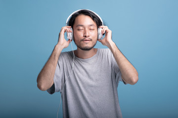 Young bearded man listening to music in blue background.