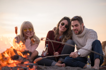 Fototapeta premium Group Of Young Friends Sitting By The Fire at beach