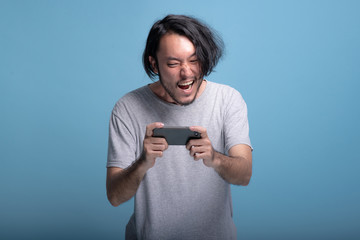 Excited Young bearded man playing mobile games in blue background.