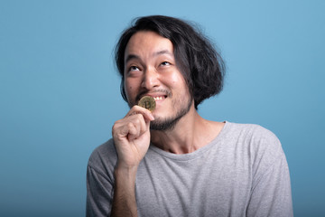 Young bearded man holding bitcoin in blue background.