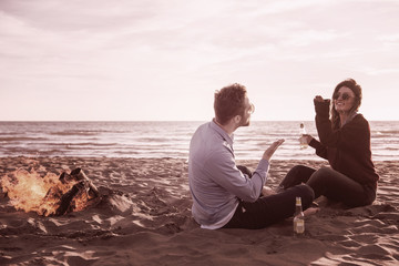 Fototapeta premium Young Couple Sitting On The Beach beside Campfire drinking beer