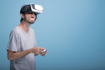 Young bearded man playing VR game in blue background.