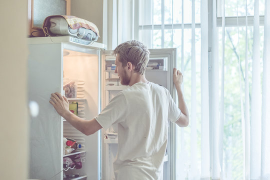 Young Handsome Bearded Man Standing Near Opended Fridge At Home Kitchen