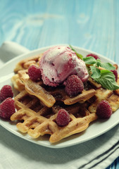 Waffles with raspberry ice cream and fresh raspberries, decorated with mint over blue wooden background