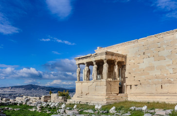 Fototapeta premium View of the Porch of the Caryatids on the Erechtheion temple on the Athens Accropolis with a view of Athens and a mountains in the background under a very blue dramatic cloudy sky