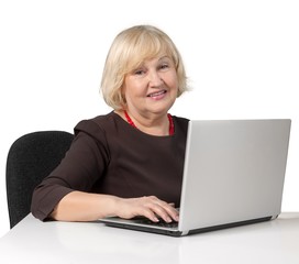 Old Woman Sitting behind Table and Typing on a Laptop - Isolated