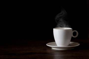A cup of hot coffee on a wooden table on black background with hot steam