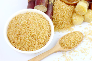 sugar cane sugar, granulated sugar brown in a white cup, granulated sugar yellow on spoon wooden over white background