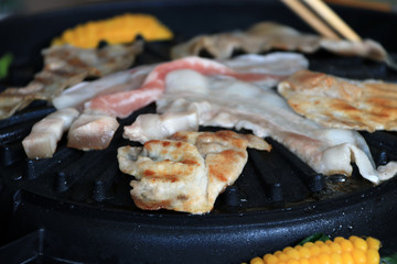 meat, bacon and streaky pork grilled on the black electric grill with corn boil at the side of it.