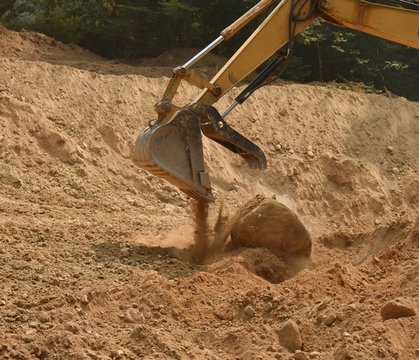 Trackhoe bucket dropping large heavy boulder