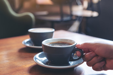 Closeup image of a hand holding a blue cup of hot coffee with smoke on wooden table in cafe