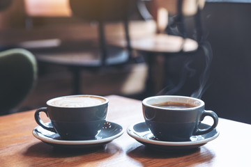 Closeup image of two blue cups of hot latte coffee and Americano coffee on vintage wooden table in...