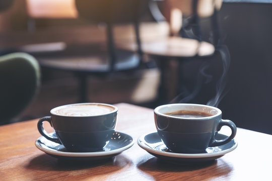 Closeup image of two blue cups of hot latte coffee and Americano coffee on vintage wooden table in cafe