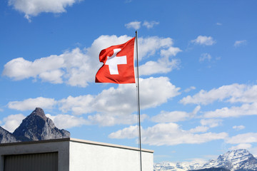 Swiss flag. Blue sky background. Sunny day with clouds. 