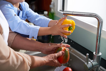 Hands of grandmother and grandson rinsing vegetables for salad