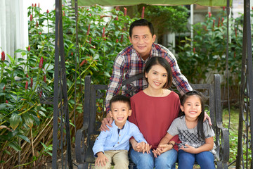 Portrait of happy Vietnamese man, his wife and children resting in backyard