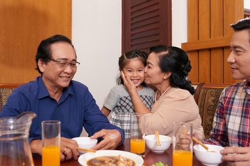 Grandmother kissing granddaughter on cheek at family dinner