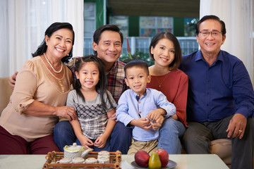 Portrait of happy big Vietnamese family sitting on sofa and smiling at camera
