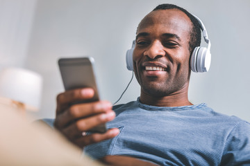 Modern life. High-spirited joyful man sitting in headphones while listening to the music