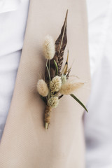 Bräutigam Ansteckblume mit Feder und getrockneten Wildblumen im Boho-Stil auf beiger Weste © Oleg Breslavtsev