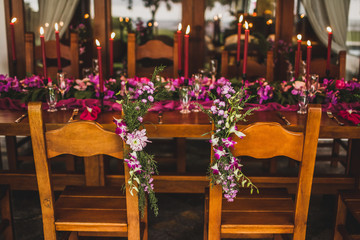 Fototapeta na wymiar Wooden wedding table decorated with red candles, pink cloth and purple orchids. Romantic family dinner in evening