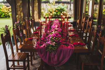 Fototapeta na wymiar Wooden wedding table decorated with red candles, pink cloth and purple orchids. Romantic family dinner in evening