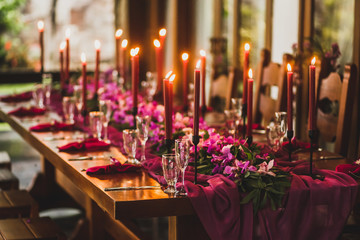Wooden wedding table decorated with red candles, pink cloth and purple orchids. Romantic family...