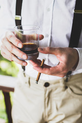 Man holding in hands glass of whisky and cigar
