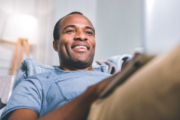 Future events. Joyful pleasant man thinking about future plans while laying on the sofa