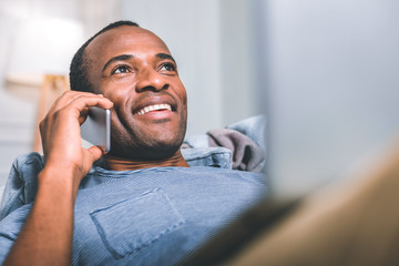 Telephone call. Excited high-spirited man speaking on the phone while laying on the sofa