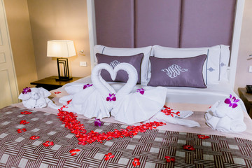 two swans made from towels are kissing on honeymoon white bed. creamy pillow and heart form, valentine signature made from red rose flower on bed decoration in bedroom.Valentine background.honey moon